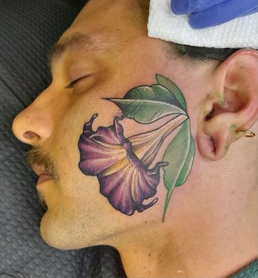 Man with a colorful flower tattoo on his face.