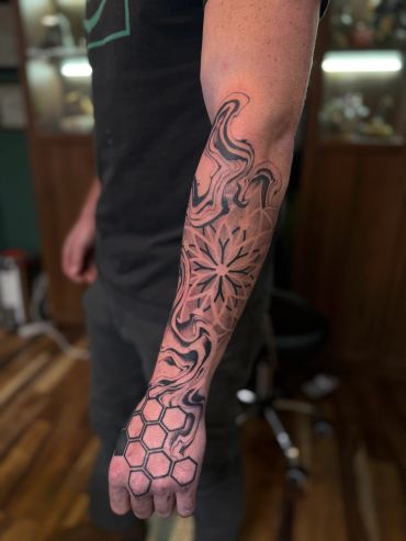 Abstract black ink tattoo with geometric and swirling patterns on forearm and hand.