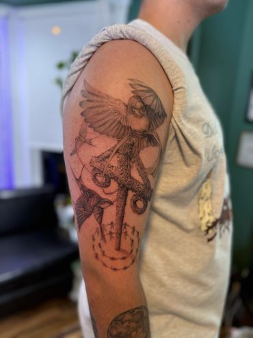 Detailed tattoo of a bird and anchor on an arm.