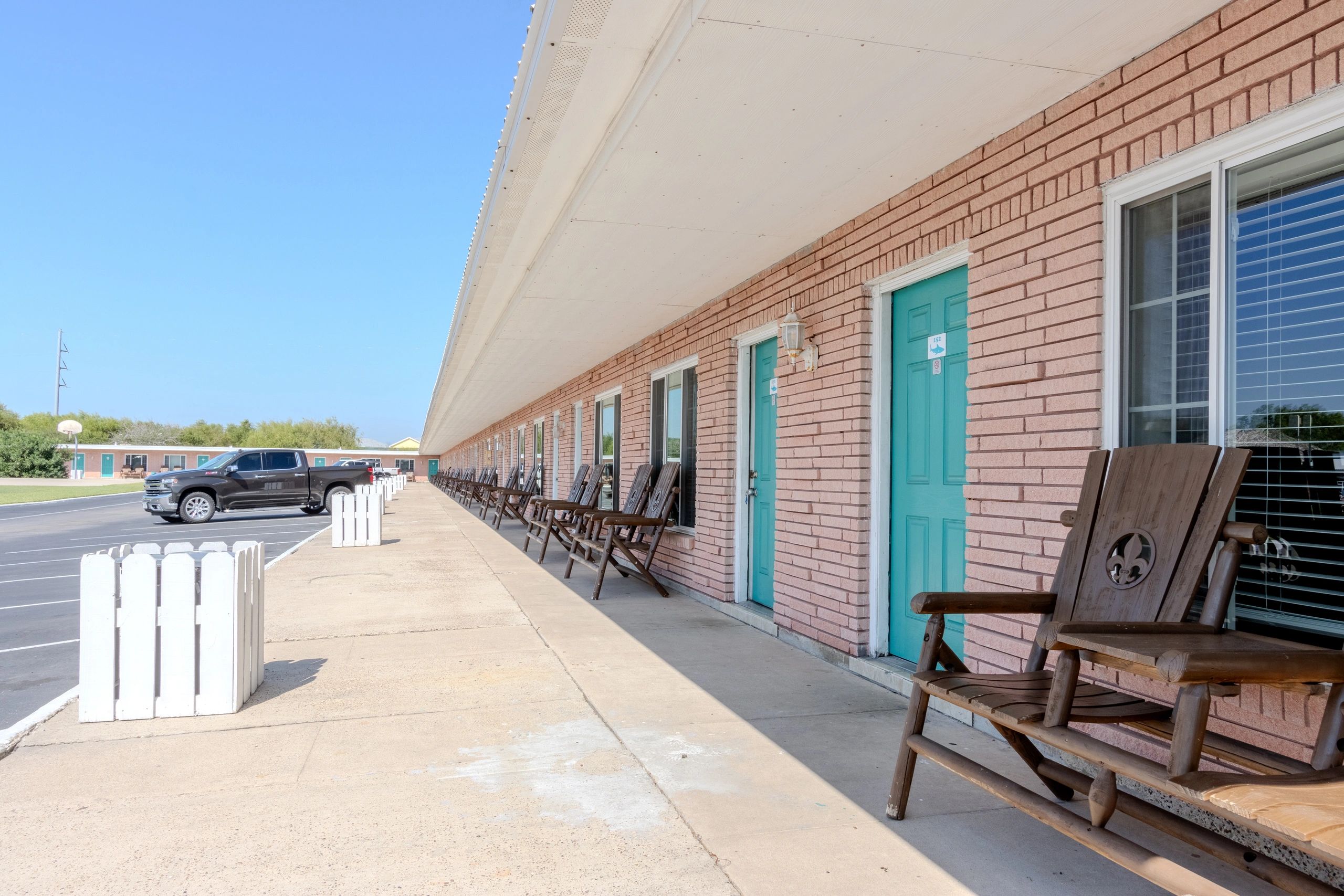 A long, low-rise brick building with teal doors and rocking chairs on the porch.