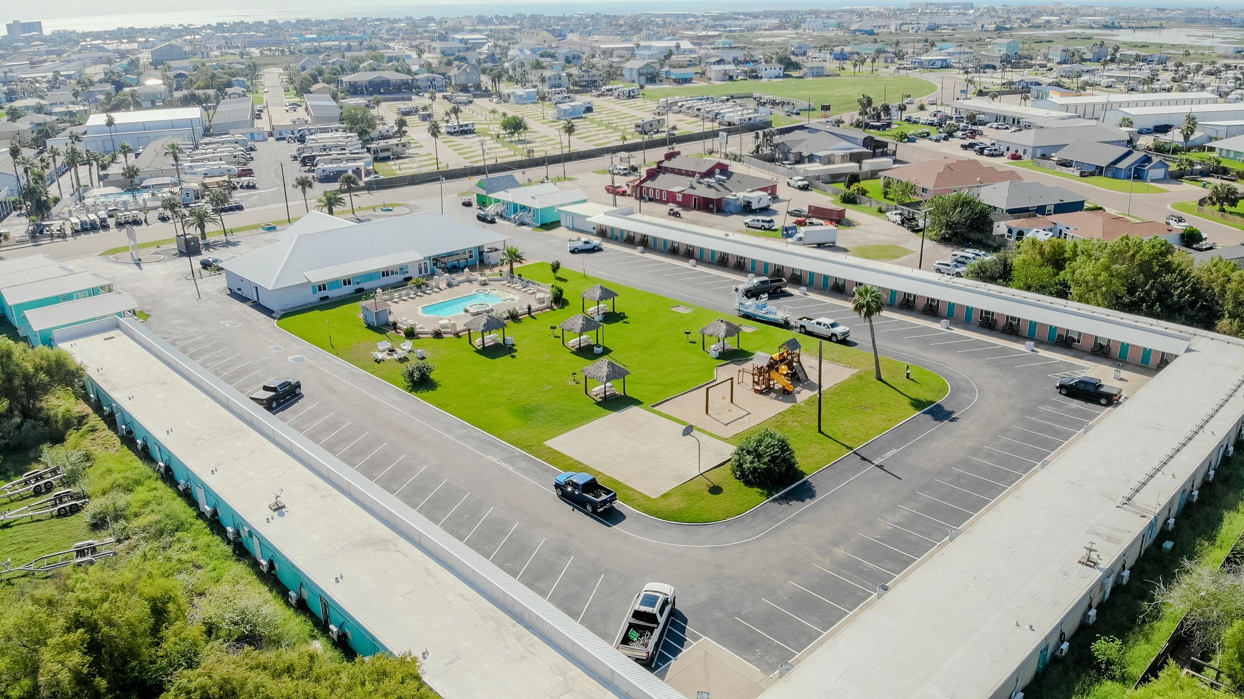 An aerial view of a hotel with a parking lot, pool, and playground.