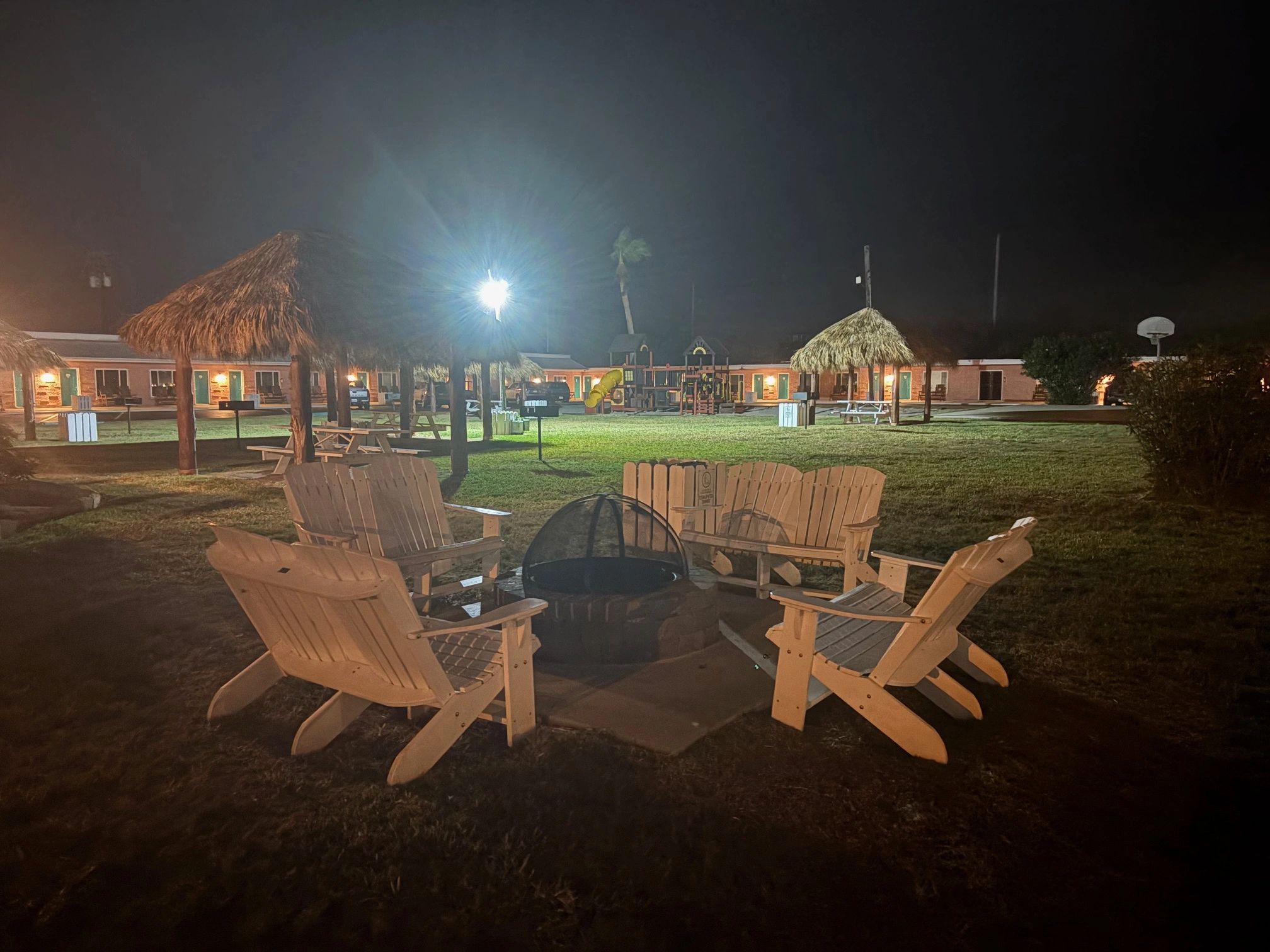 a fire pit with wooden chairs around it in a grassy area at night