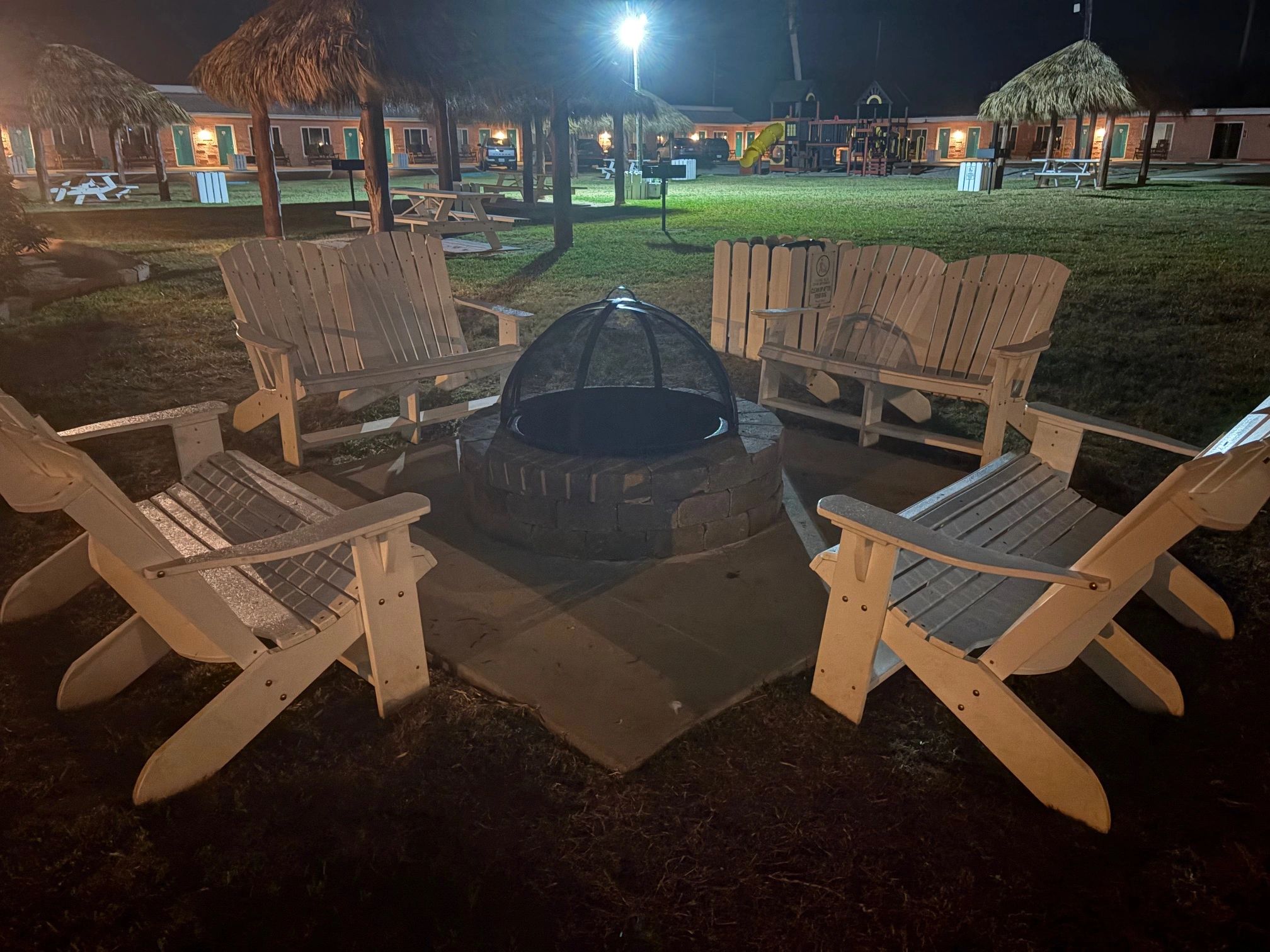 A fire pit with wooden chairs around it in a grassy area at night.