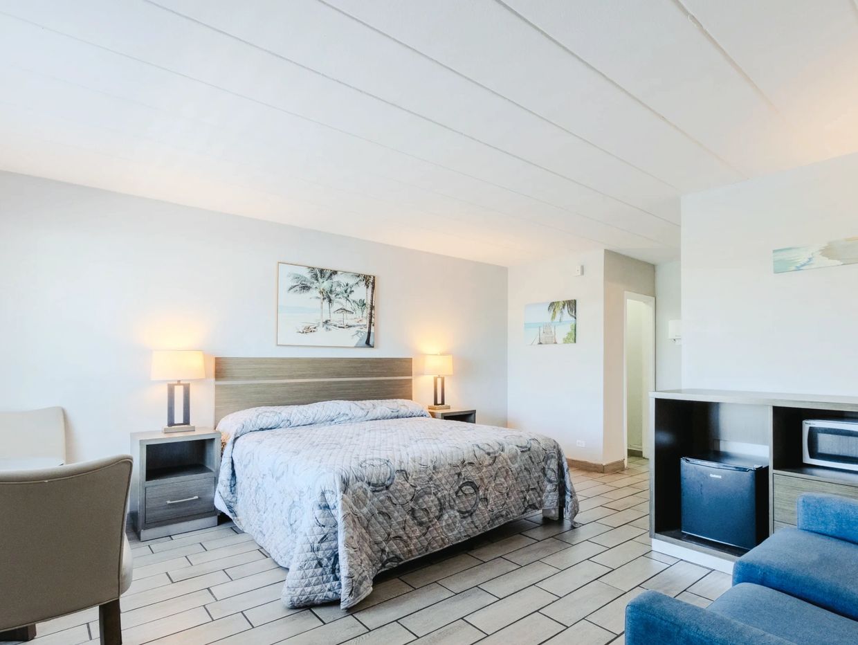 A hotel room with a bed, nightstands, a chair, and a mini fridge with microwave
