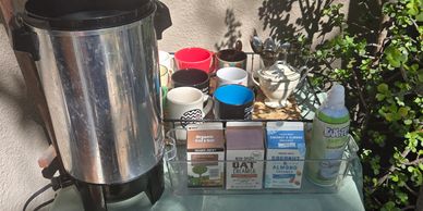 A beverage station with cups, drink cartons, and a large dispenser outdoors.
