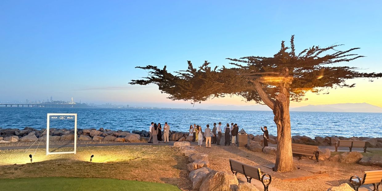 Waterfront view at Hong Kong East Ocean with tree, benches, and Bay Bridge in background.