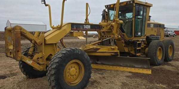 A yellow Caterpillar 140H motor grader in a field.