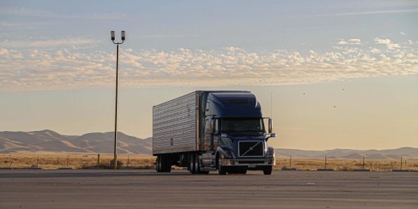 A large black semi-truck parked in an empty lot near desert mountains.