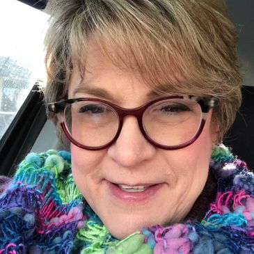 Smiling woman wearing glasses and a colorful scarf inside a car.
