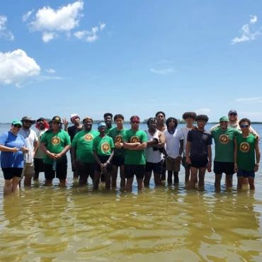 Group of people standing in shallow water under a bright sky.