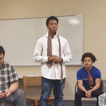 Three young men in a classroom setting, two wearing neckties.