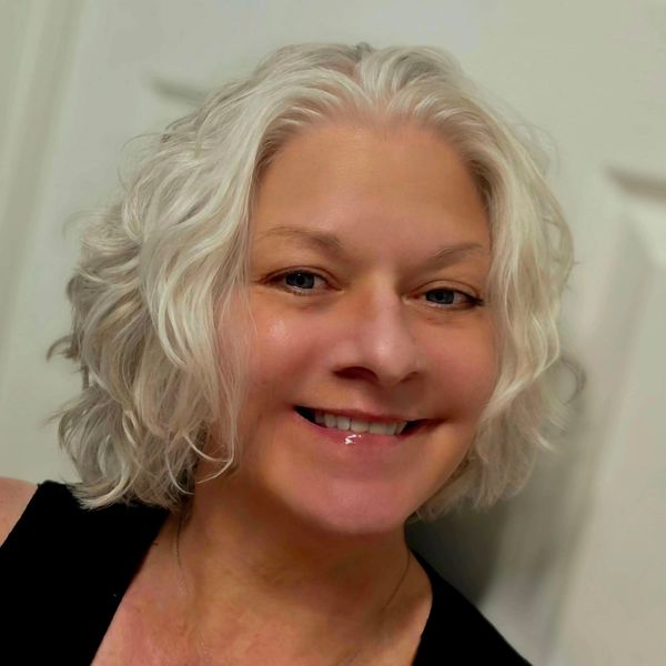 Smiling woman with short, wavy white hair and a black top.
