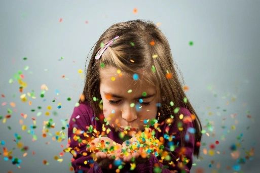 Girl blowing colorful confetti from her hands.