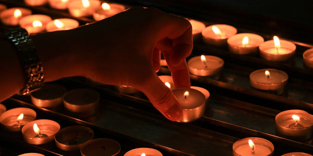 Hand placing a lit tealight candle among many others in a dark setting.