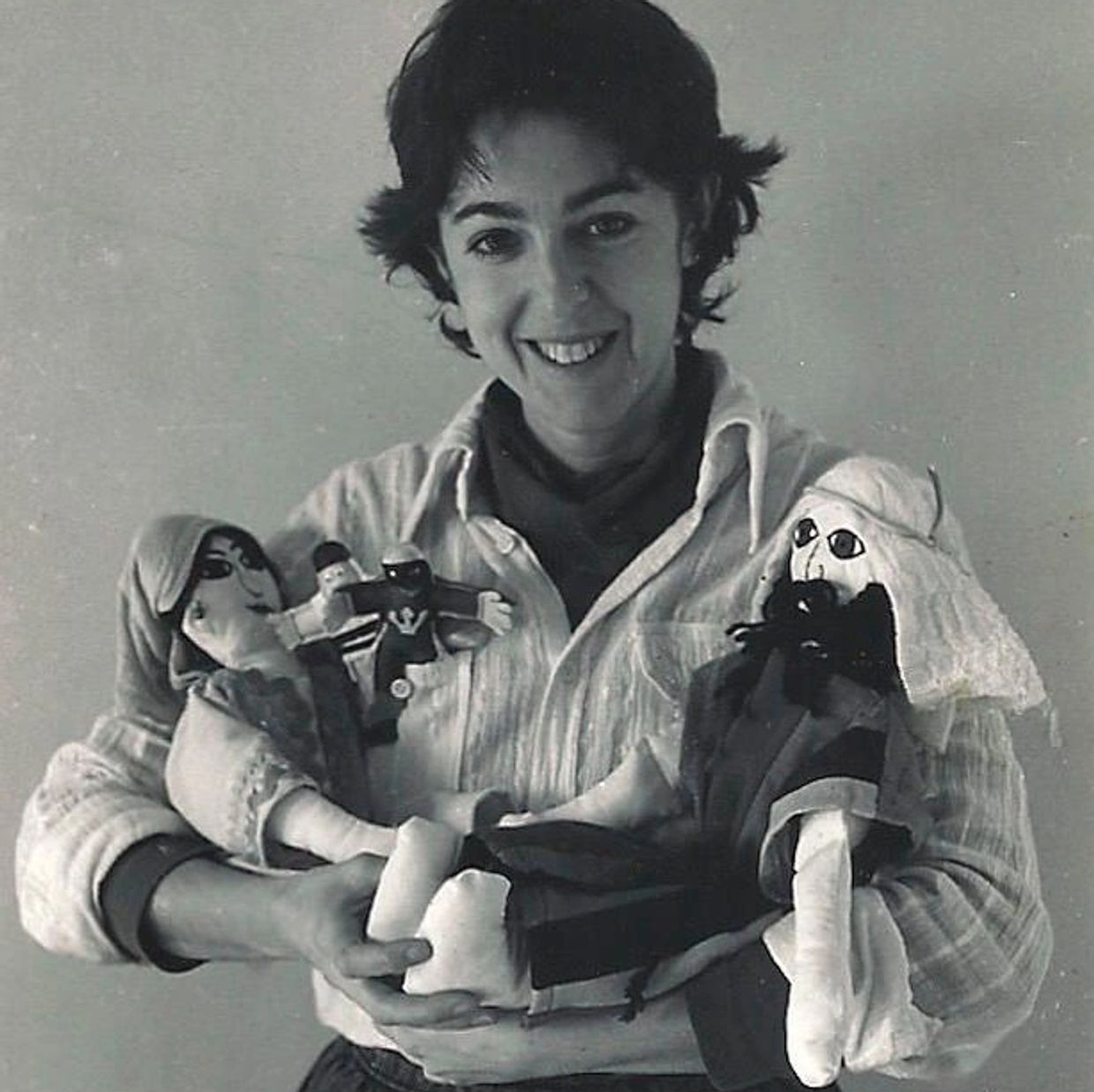 Smiling woman holding two handmade dolls in black and white photo.