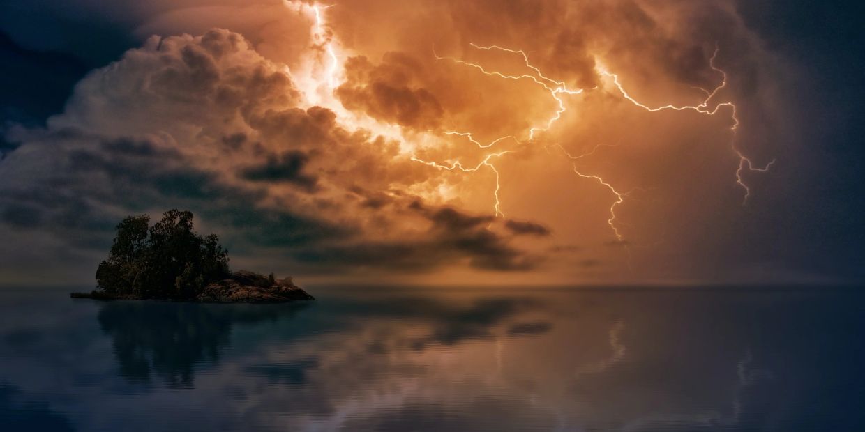 Lightning illuminates a small island amid a stormy sky.