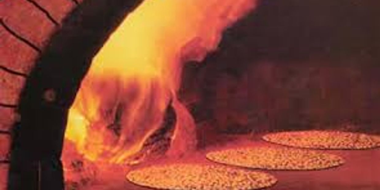 Three pizzas baking in a wood-fired oven with visible flames.