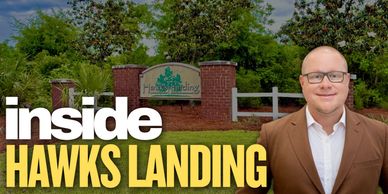 Man in brown blazer stands in front of Hawks Landing sign in a green park.