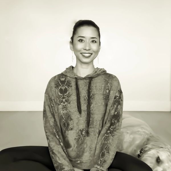 Smiling woman sitting cross-legged indoors with a dog beside her.