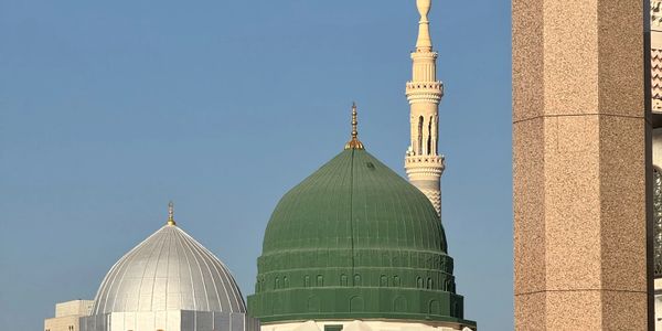 Green and silver domes with a minaret against a clear blue sky.