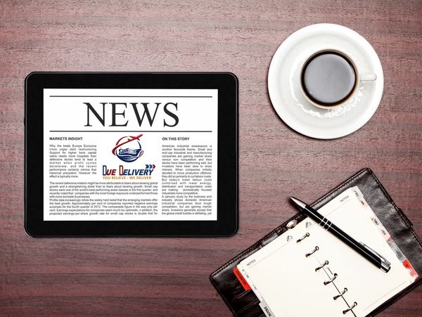 Tablet showing news, coffee cup, and open planner with pen on wooden table.