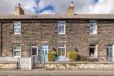 Stone terraced houses with distinct chimneys under a partly cloudy sky.