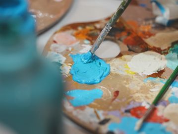 Paintbrush dipped in bright blue paint on an artist's palette.