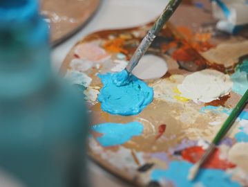 Paintbrush dipped in bright blue paint on an artist's palette.