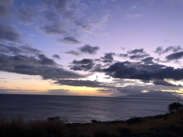 Sunset over the ocean with dramatic clouds and a calm sea from the Maui overlook for whale spotting.