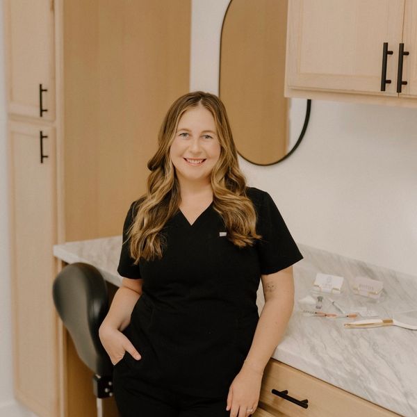 Smiling woman in black scrubs leaning on a marble countertop in a modern room.