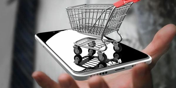A miniature shopping cart on a smartphone held by a person.