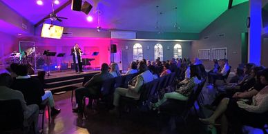 A speaker addresses an audience in a colorful, dimly lit room.