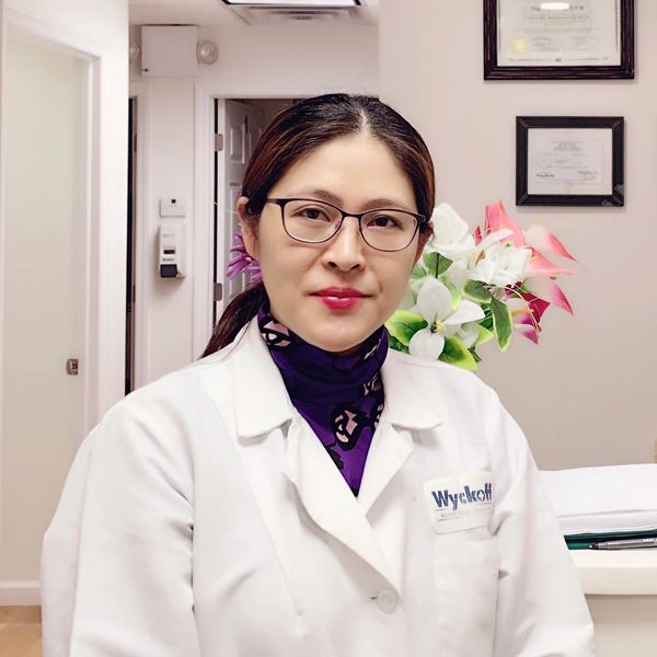 A female doctor in a white coat with glasses sitting in an office.