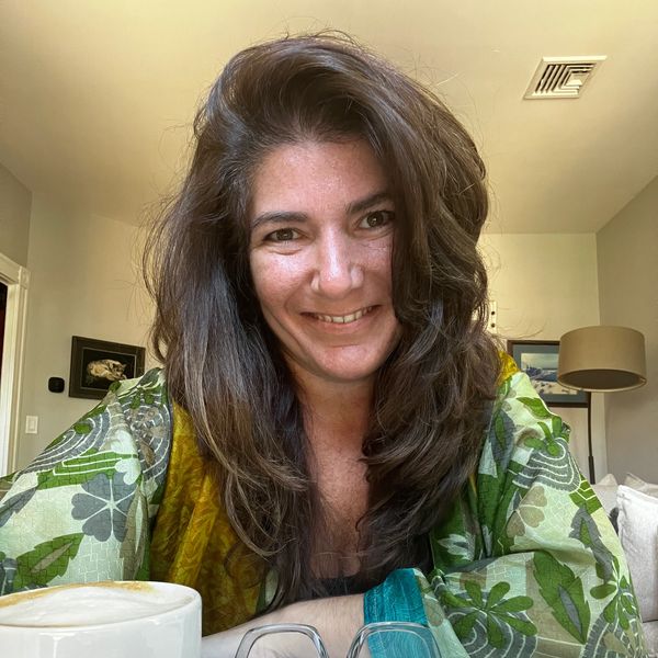 Smiling woman in a green patterned blouse sitting at a table with coffee and glasses.