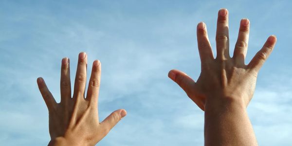 Two hands with fingers spread against a blue sky.