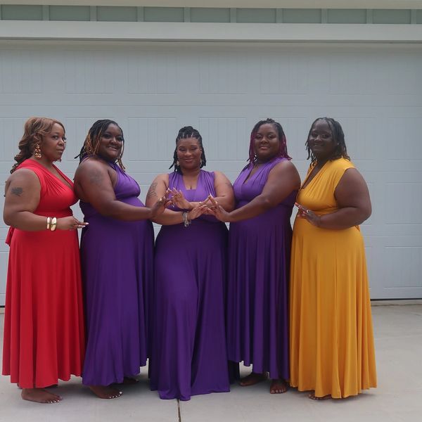 Five women in colorful dresses posing together in front of a garage door.