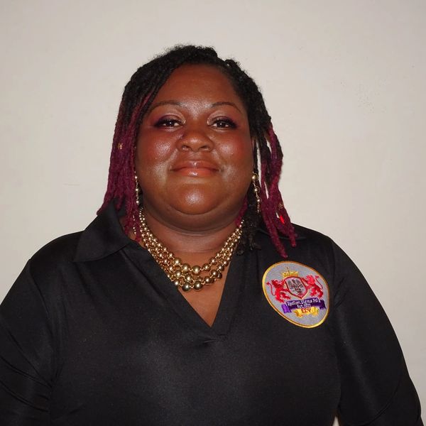 Smiling woman wearing a black shirt with a colorful emblem and gold necklace.