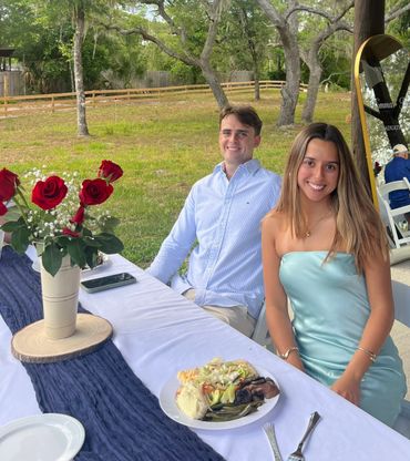 Young couple sitting at a decorated outdoor table with food and roses.