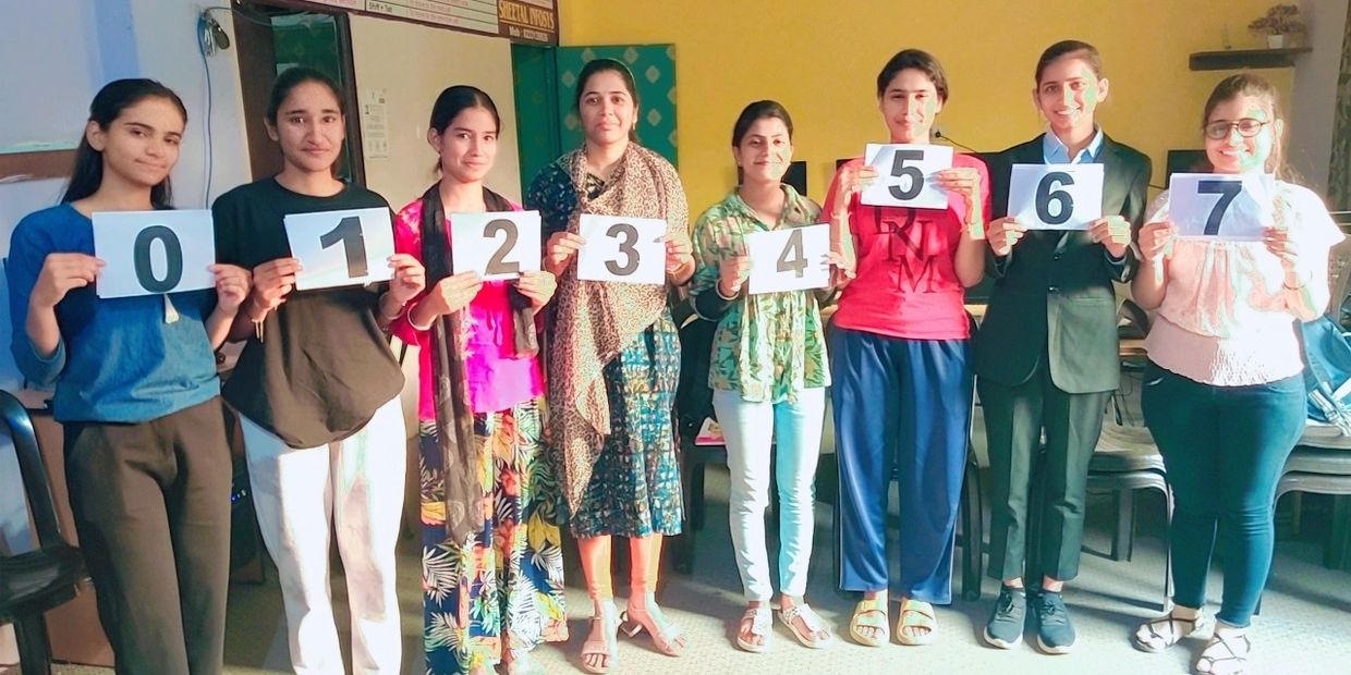 Eight people holding cards with numbers 0 to 7, standing in a row indoors.