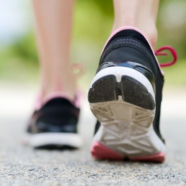 Close-up of a person walking in black and pink sneakers on a path.