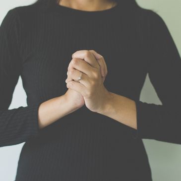Person with clasped hands wearing a ring on finger.