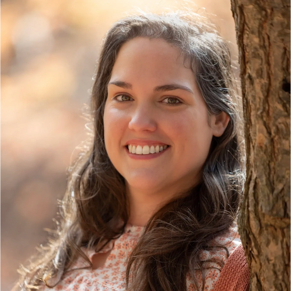 Top half view of the owner of Sweet Pea Bookkeeping leaning on a tree while smiling at the camera.