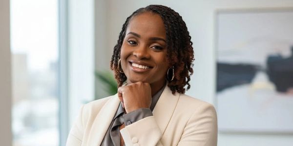 Confident professional woman in a white blazer smiling at the camera in an office.