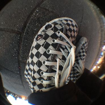 Worn checkered shoe with holes on black pavement at night.