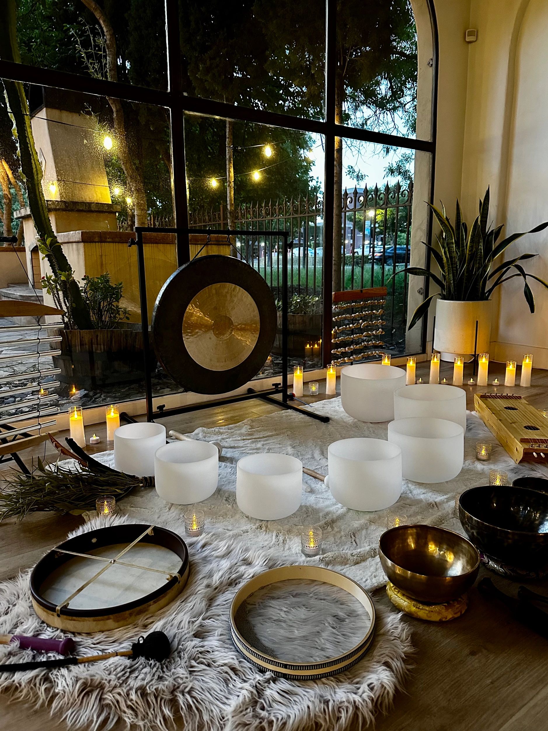 A serene music and meditation setup with singing bowls, a gong, candles, and plants.