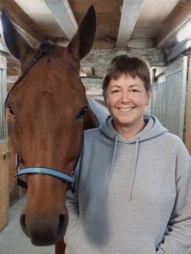 A woman smiling beside a brown horse in a stable.