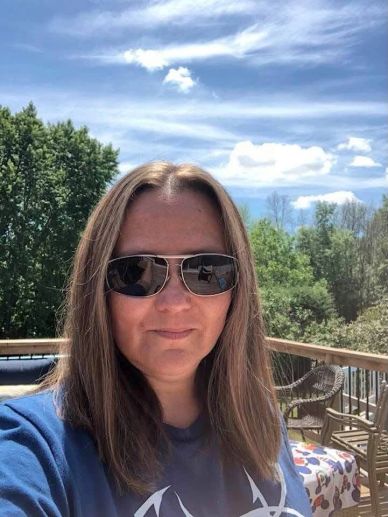Woman wearing sunglasses outdoors with a scenic sky background.