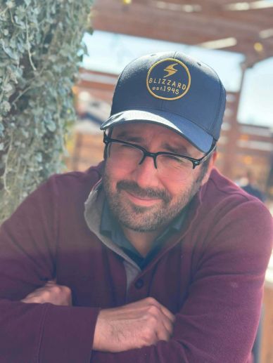 Man wearing a Blizzard cap and glasses, smiling warmly.