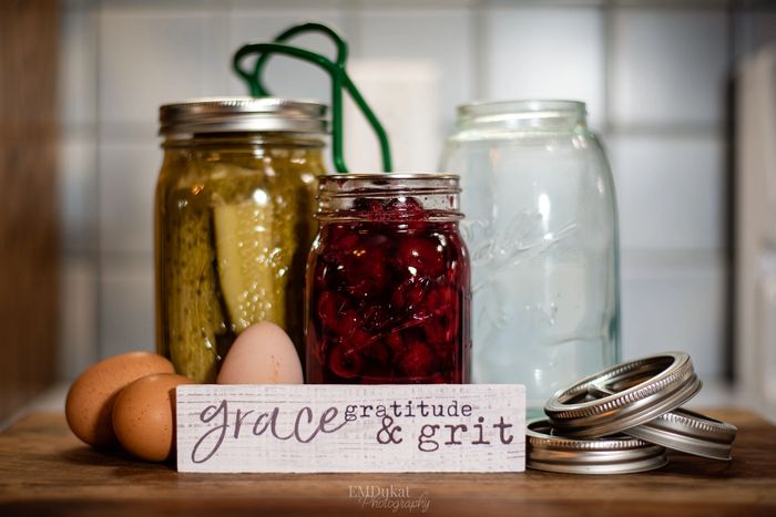 Collection of canning jars, tools, lids, farm fresh eggs, sign that says grace, gratitude and grit