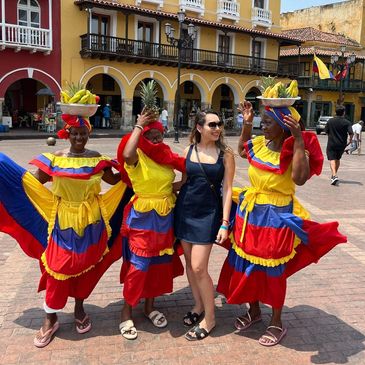 A woman with three dancers in colorful traditional Colombian dresses in a plaza.